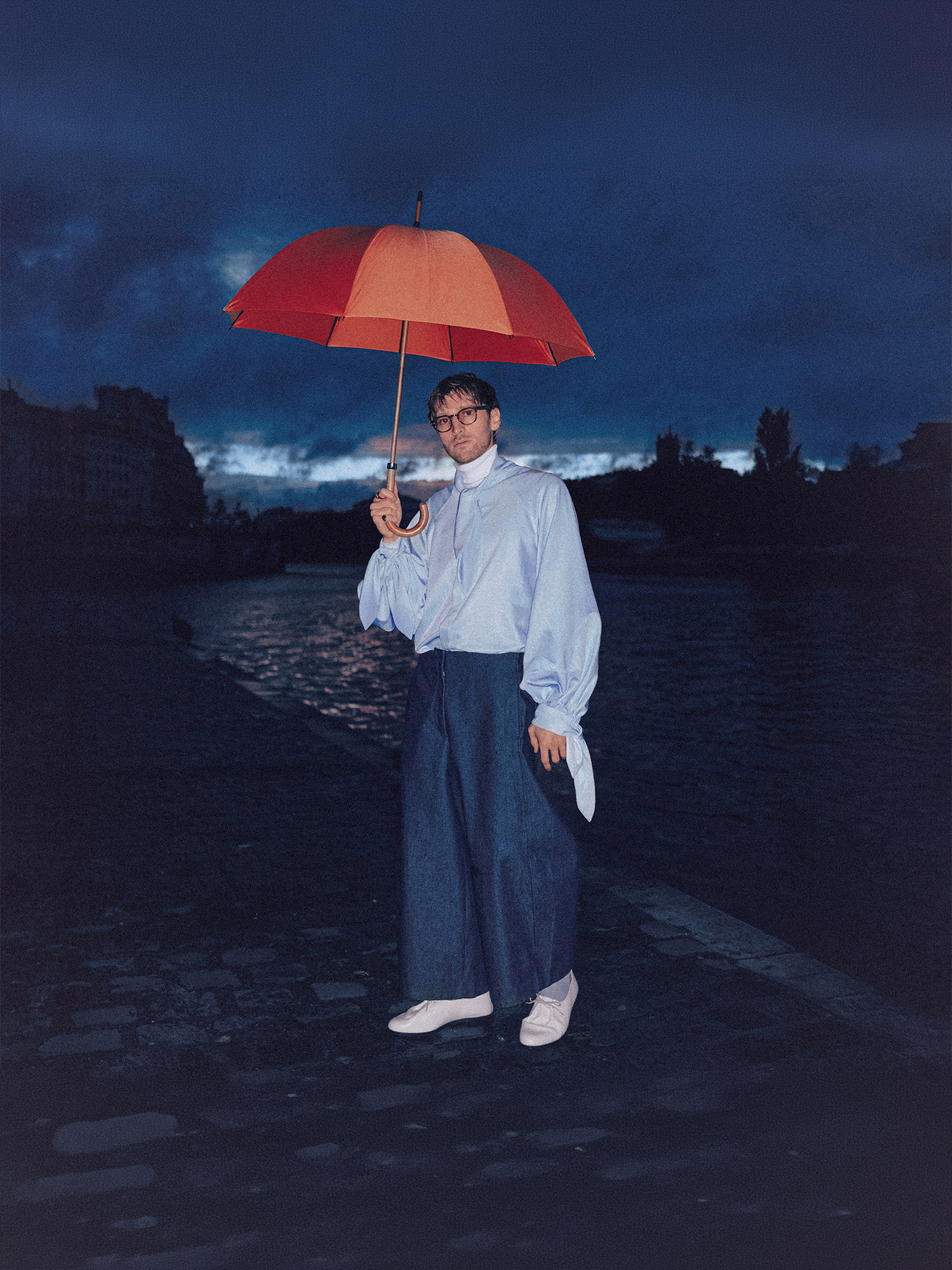 Mathis Riviere sous un parapluie orange, sur les quais de Seine à la tombée de la nuit